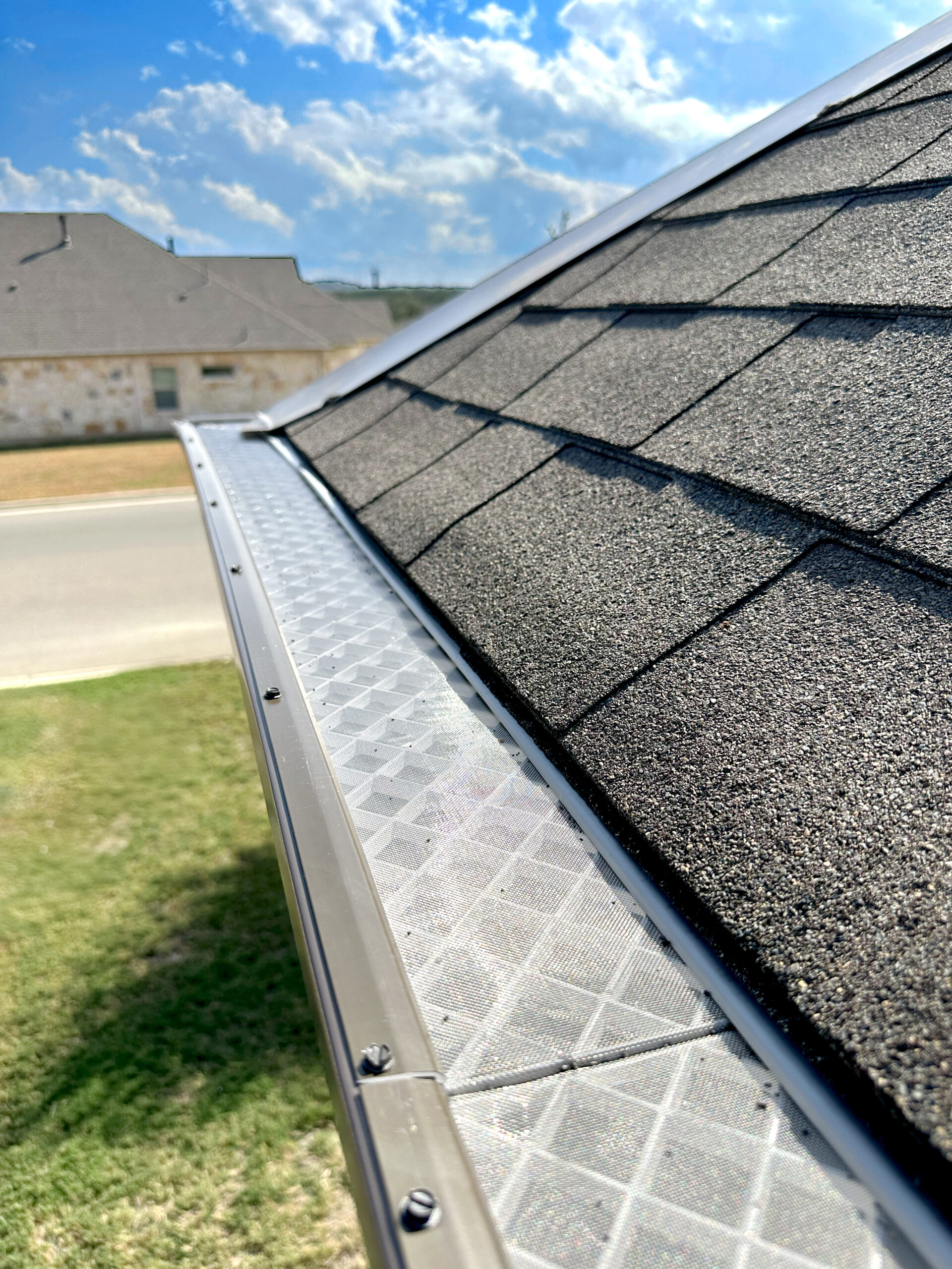 Close-up of a gutter guard installed along a shingle roof edge